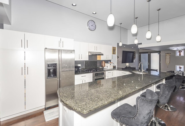 kitchen featuring a high ceiling, pendant lighting, appliances with stainless steel finishes, white cabinetry, and sink