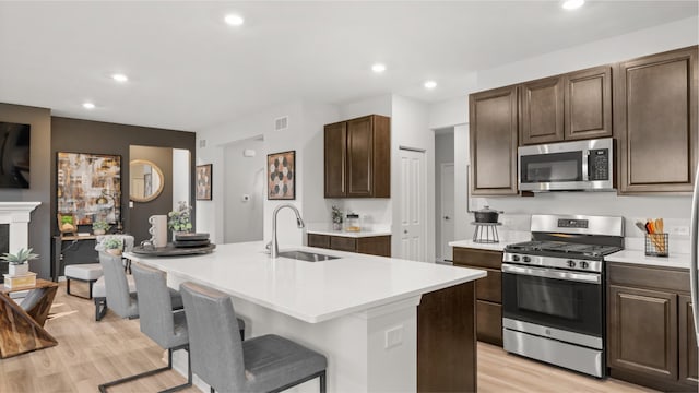 kitchen with a breakfast bar, a kitchen island with sink, sink, light hardwood / wood-style flooring, and appliances with stainless steel finishes