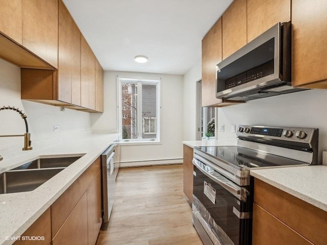 kitchen with light wood-type flooring, light stone counters, stainless steel appliances, sink, and a baseboard radiator