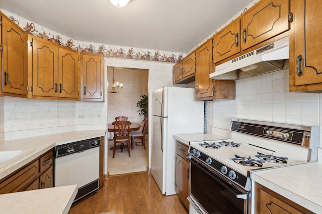 kitchen with light wood-type flooring, white appliances, a chandelier, and backsplash