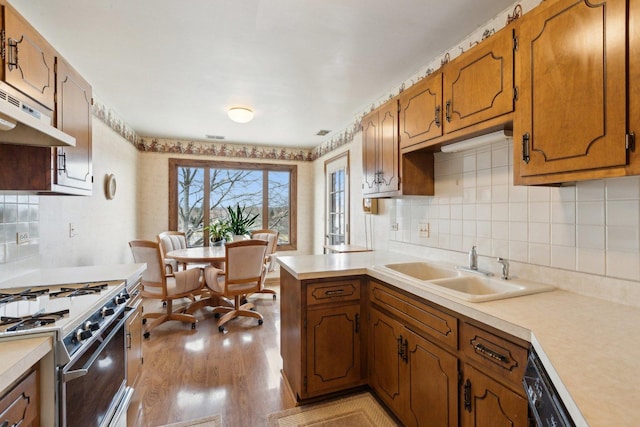 kitchen with sink, gas range oven, backsplash, kitchen peninsula, and light wood-type flooring