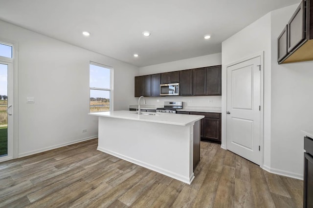 kitchen featuring sink, an island with sink, stainless steel appliances, and hardwood / wood-style flooring