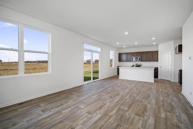 kitchen with dark brown cabinets, light wood-type flooring, plenty of natural light, and an island with sink