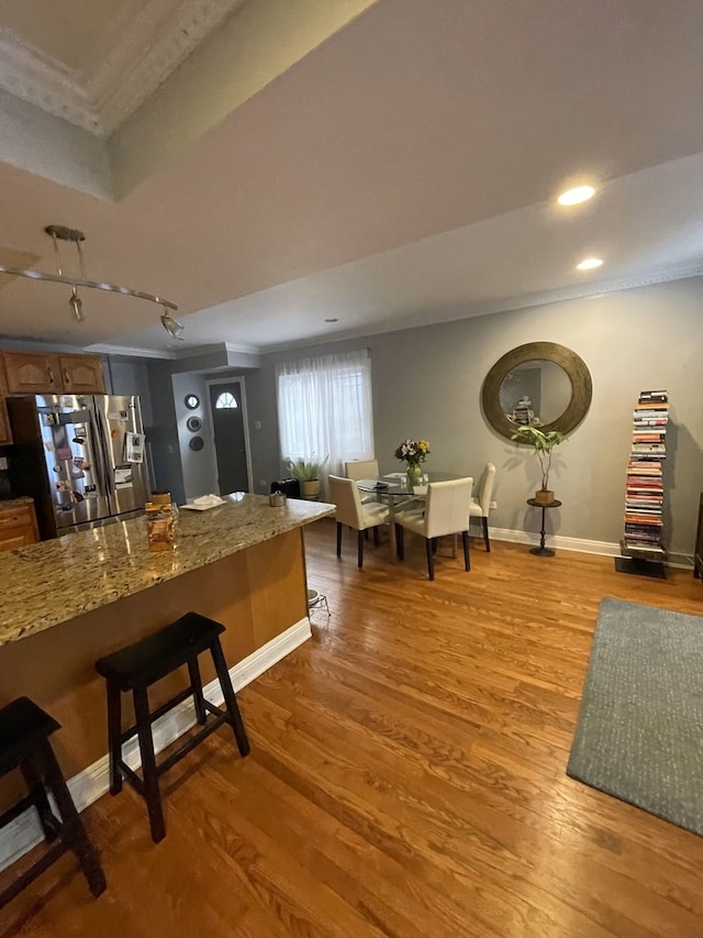 kitchen featuring stainless steel fridge with ice dispenser, stone countertops, light hardwood / wood-style flooring, and a breakfast bar area