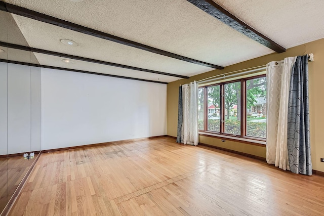 unfurnished room featuring beam ceiling, a textured ceiling, and wood-type flooring