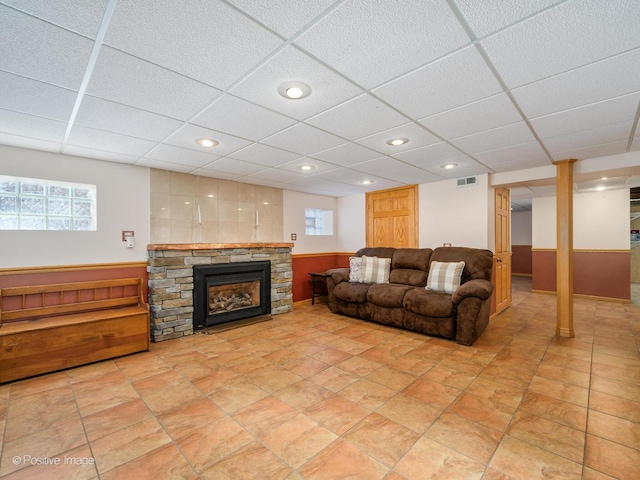 living room featuring wood walls, a drop ceiling, and a stone fireplace