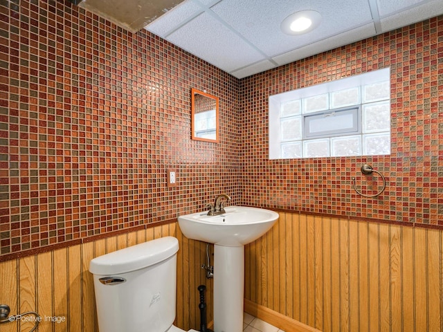 bathroom with toilet, a paneled ceiling, sink, and wood walls