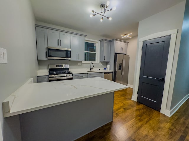 kitchen featuring light stone countertops, gray cabinetry, stainless steel appliances, sink, and an inviting chandelier