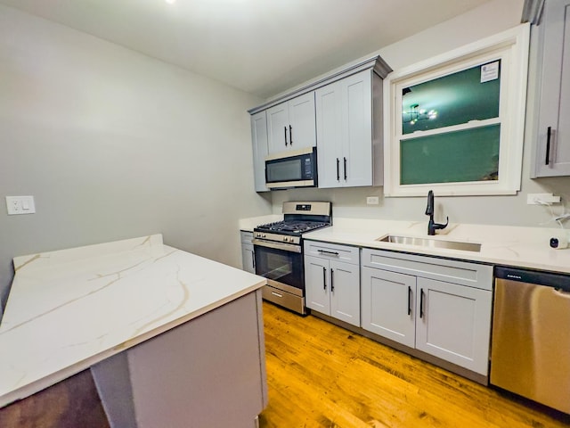 kitchen with appliances with stainless steel finishes, light wood-type flooring, light stone counters, sink, and gray cabinets