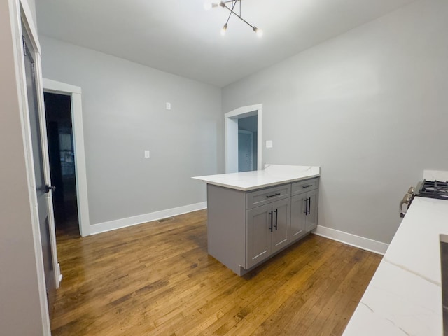 kitchen with gray cabinetry, kitchen peninsula, hardwood / wood-style floors, and a chandelier