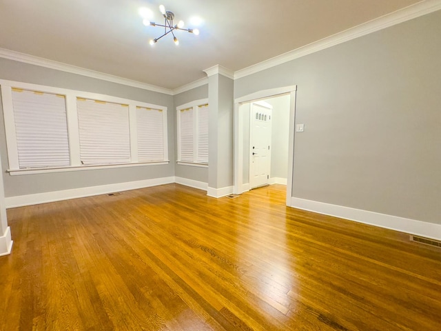 empty room with hardwood / wood-style flooring, ornamental molding, and a notable chandelier