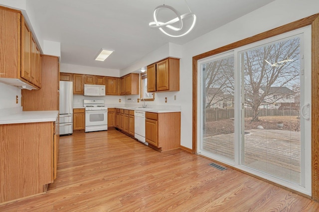 kitchen with sink, white appliances, decorative light fixtures, and light hardwood / wood-style floors