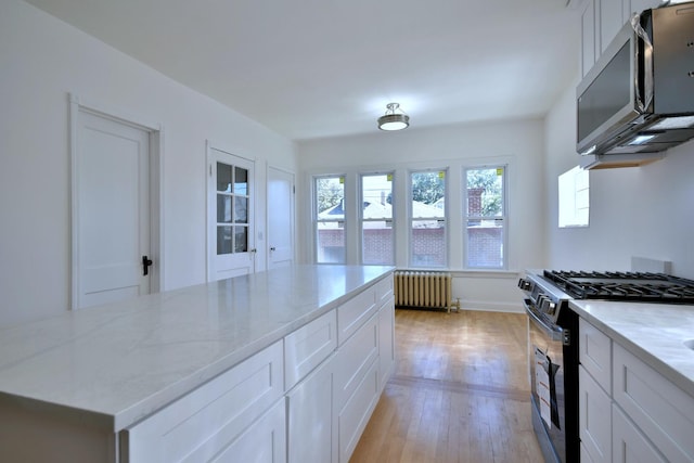 kitchen with radiator, white cabinets, light hardwood / wood-style flooring, light stone countertops, and stainless steel appliances