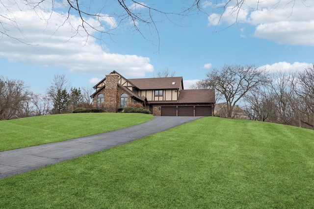 tudor-style house featuring driveway, a shingled roof, stone siding, a front lawn, and stucco siding