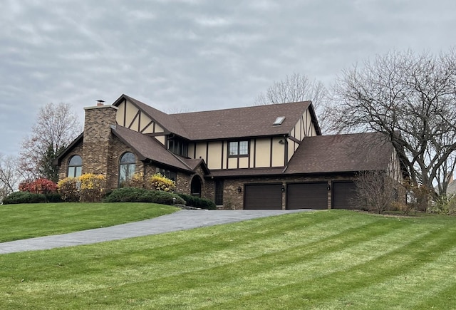 english style home featuring a chimney, stucco siding, a shingled roof, a front yard, and driveway