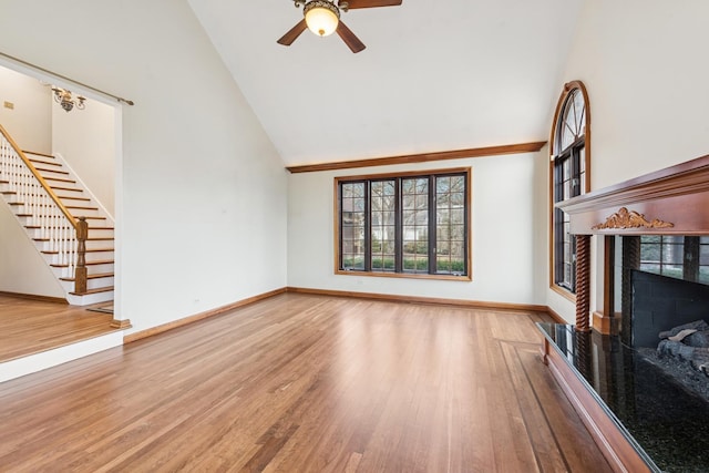 unfurnished living room featuring baseboards, stairway, wood finished floors, a fireplace, and high vaulted ceiling