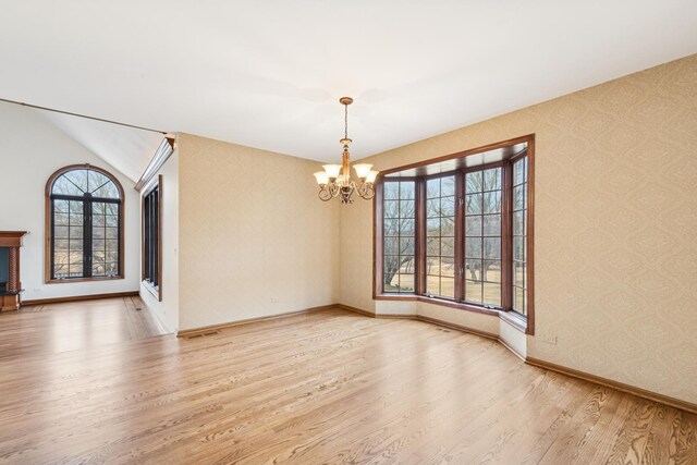 unfurnished dining area with a notable chandelier, baseboards, wood finished floors, and wallpapered walls