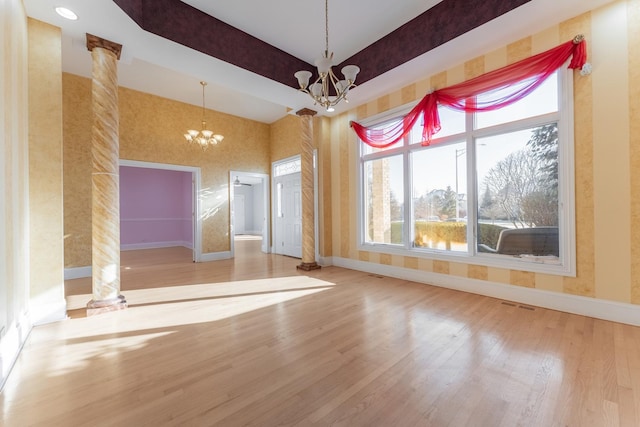 unfurnished room with ornate columns, hardwood / wood-style floors, and an inviting chandelier