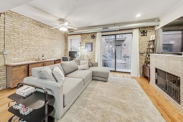 living room featuring light wood-type flooring, ceiling fan, crown molding, and brick wall