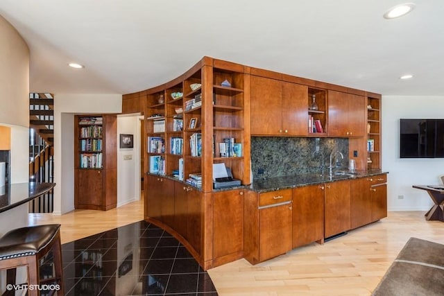 kitchen with dark stone countertops, sink, backsplash, and light hardwood / wood-style flooring