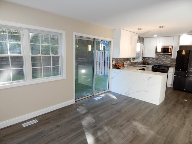 kitchen featuring white cabinetry, hanging light fixtures, light stone counters, plenty of natural light, and black refrigerator