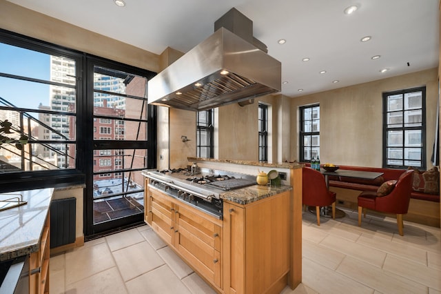 kitchen with stainless steel gas stovetop, island range hood, plenty of natural light, and dark stone counters