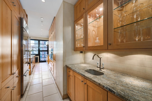 bar with decorative backsplash, light stone counters, sink, oven, and light tile patterned flooring