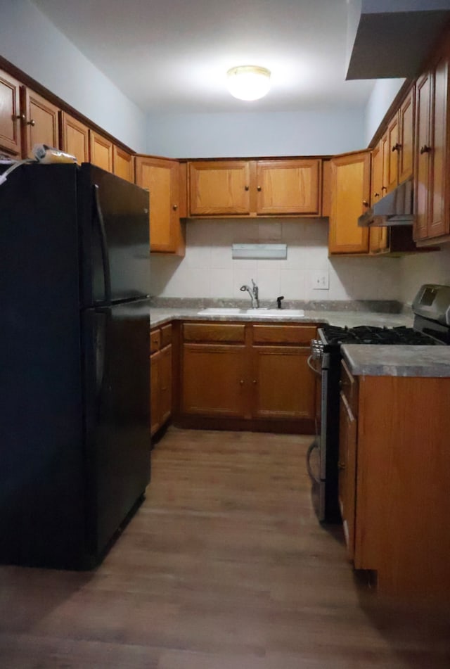 kitchen with sink, backsplash, hardwood / wood-style flooring, black fridge, and stainless steel gas range