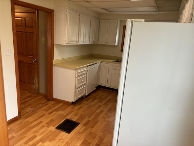 kitchen with white appliances, light hardwood / wood-style floors, white cabinetry, and a drop ceiling