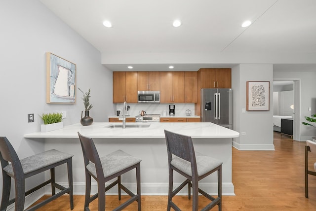 kitchen featuring a breakfast bar, light countertops, appliances with stainless steel finishes, brown cabinetry, and a sink