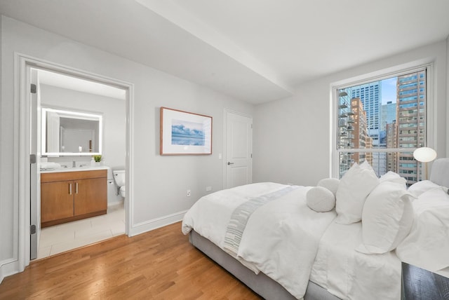 bedroom featuring baseboards, a city view, connected bathroom, and light wood-style floors