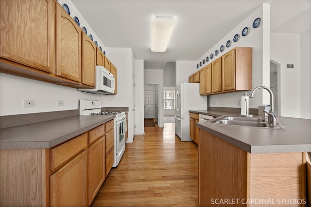 kitchen featuring dark countertops, white appliances, a sink, and light wood-style flooring