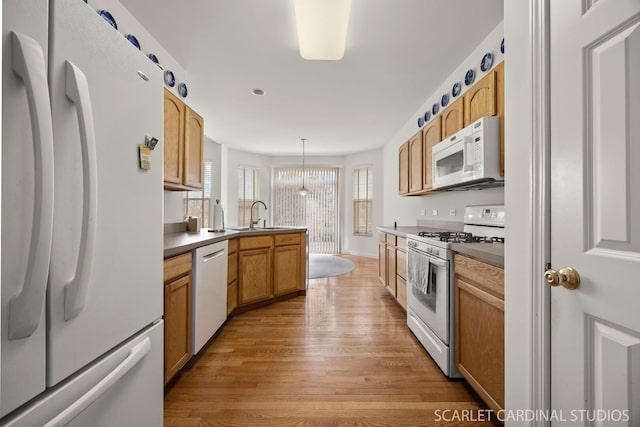 kitchen with decorative light fixtures, light wood finished floors, a sink, white appliances, and a peninsula