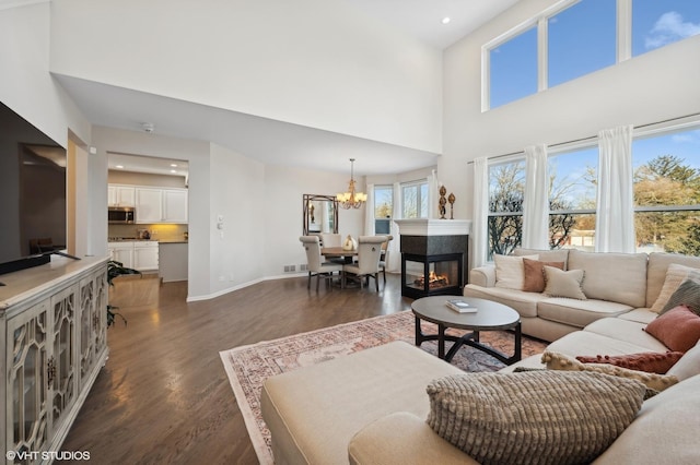 living room with a multi sided fireplace, a towering ceiling, dark hardwood / wood-style floors, and a notable chandelier