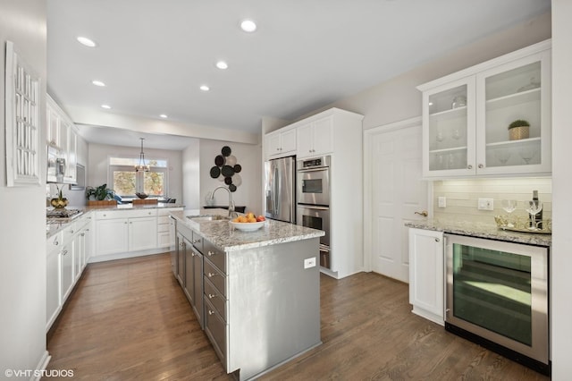 kitchen with wine cooler, a center island with sink, sink, white cabinetry, and stainless steel appliances