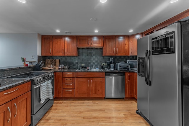 kitchen featuring dark stone counters, sink, light hardwood / wood-style flooring, decorative backsplash, and appliances with stainless steel finishes