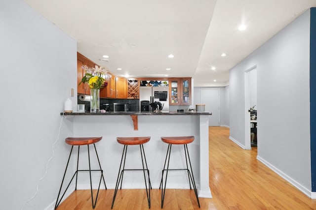 kitchen featuring kitchen peninsula, stainless steel fridge with ice dispenser, dark stone countertops, and light hardwood / wood-style floors