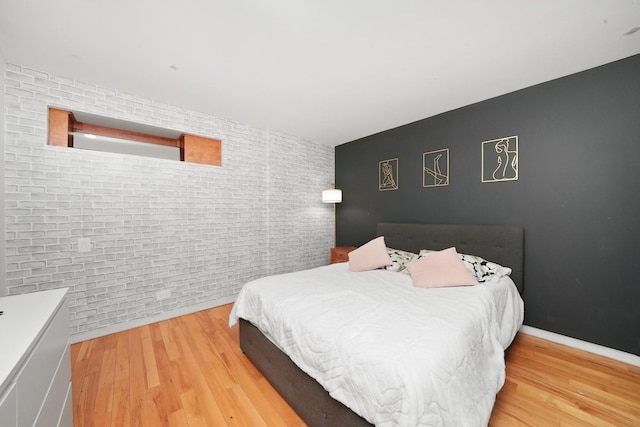 bedroom featuring wood-type flooring and brick wall