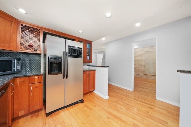 kitchen with decorative backsplash, brick wall, light wood-type flooring, and appliances with stainless steel finishes