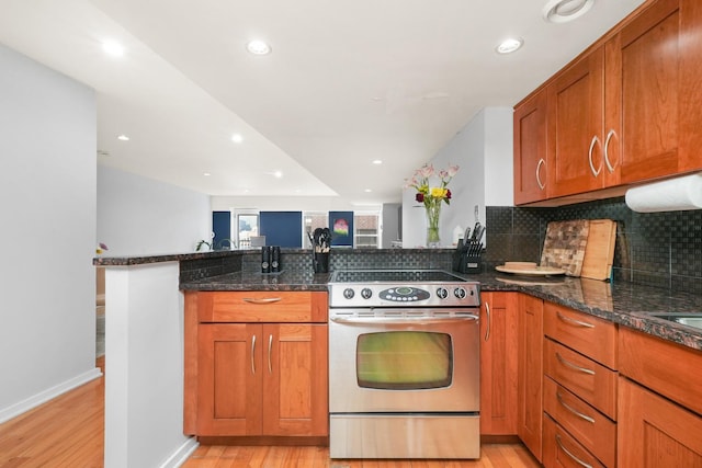 kitchen with kitchen peninsula, light hardwood / wood-style flooring, dark stone counters, and stainless steel range with electric stovetop