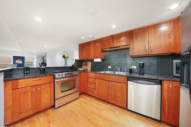 kitchen with decorative backsplash, appliances with stainless steel finishes, sink, light hardwood / wood-style flooring, and dark stone countertops