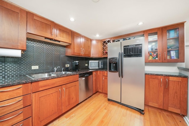 kitchen featuring sink, backsplash, dark stone counters, light hardwood / wood-style floors, and appliances with stainless steel finishes