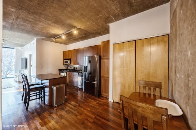 kitchen with dark wood-type flooring, stainless steel appliances, track lighting, a breakfast bar area, and a kitchen island