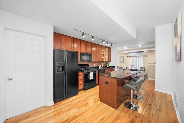 kitchen featuring a center island, black appliances, a kitchen breakfast bar, rail lighting, and light hardwood / wood-style floors