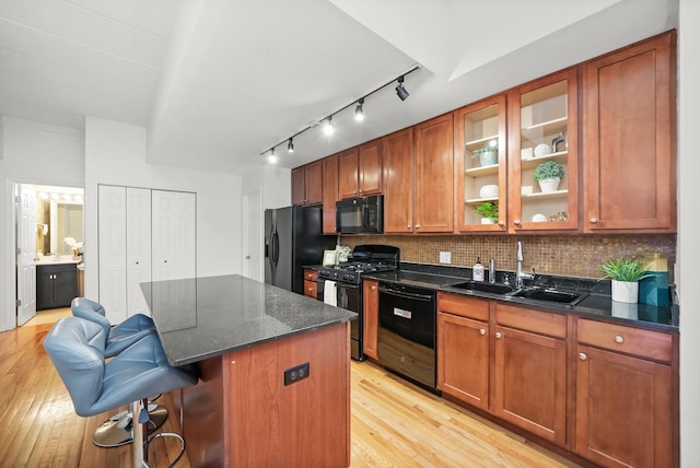 kitchen featuring sink, light hardwood / wood-style floors, a breakfast bar area, decorative backsplash, and black appliances