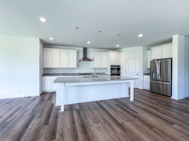 kitchen featuring wall chimney exhaust hood, white cabinetry, an island with sink, and appliances with stainless steel finishes