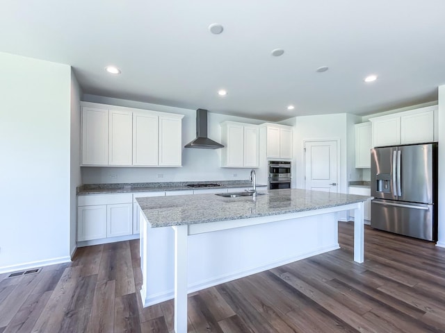 kitchen with sink, stainless steel appliances, wall chimney range hood, a kitchen island with sink, and white cabinets