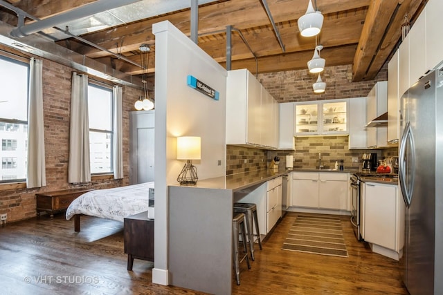 kitchen featuring beam ceiling, stainless steel refrigerator, hanging light fixtures, brick wall, and white cabinets