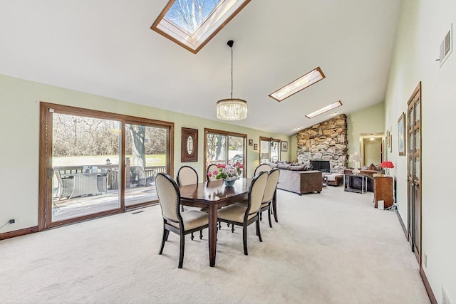 dining space featuring a skylight, light colored carpet, high vaulted ceiling, a notable chandelier, and a stone fireplace