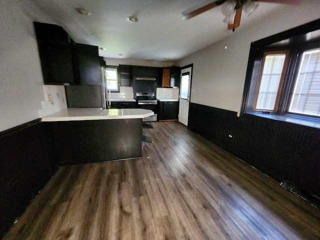 kitchen with electric range, dark hardwood / wood-style flooring, backsplash, kitchen peninsula, and a breakfast bar area